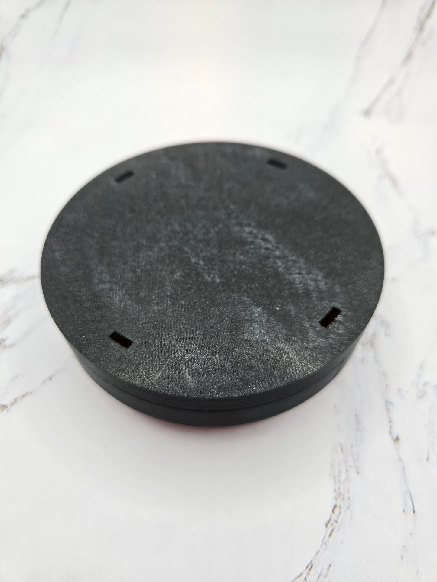 Bottom view of 3D printed Try Me animatronic step pad button showing black PETG base on marble surface