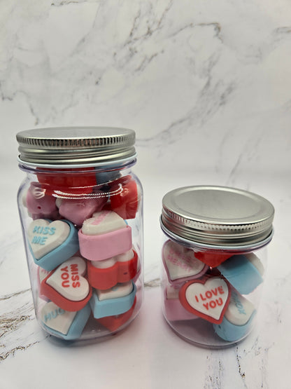 Two jars of 3D printed conversation heart fidget clickers in large and small sizes showing colorful hearts with messages like Kiss Me Miss You and I Love You Valentine's Day sensory toy gift set