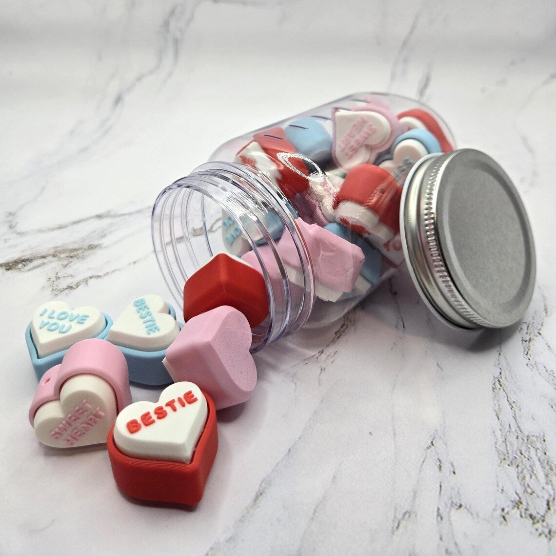 3D printed conversation heart fidget clickers spilling out of jar showing colorful hearts with messages like Bestie I Love You and Sweetheart Valentine's Day sensory toy gift clicky stress relief fidget toy